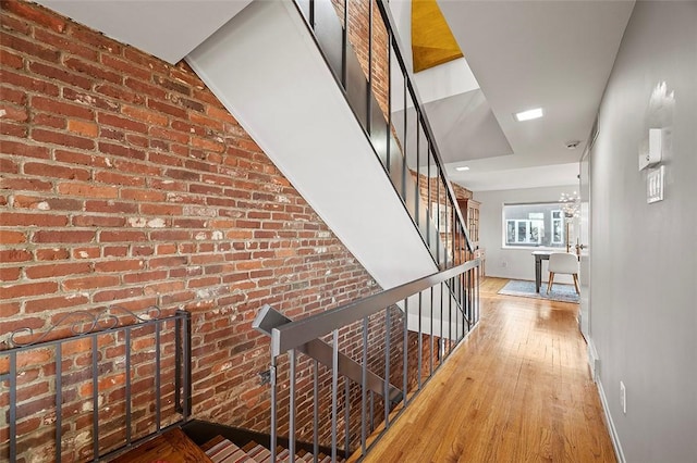 hallway with hardwood / wood-style flooring, brick wall, and an inviting chandelier