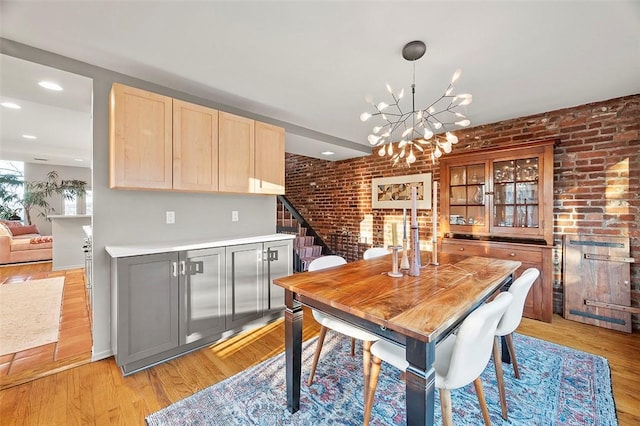 dining space featuring brick wall, a chandelier, and light hardwood / wood-style flooring