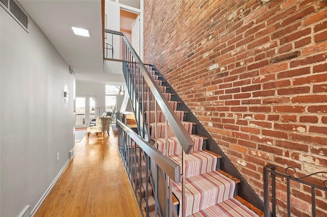 stairs featuring a high ceiling, wood-type flooring, and brick wall