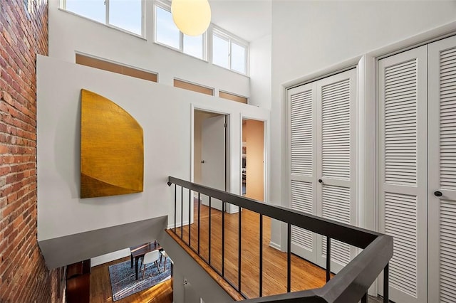 hallway with hardwood / wood-style flooring, brick wall, and a towering ceiling