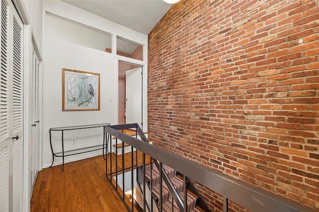 hallway featuring dark wood-type flooring and brick wall