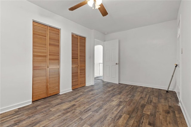 unfurnished bedroom featuring two closets, dark hardwood / wood-style floors, and ceiling fan