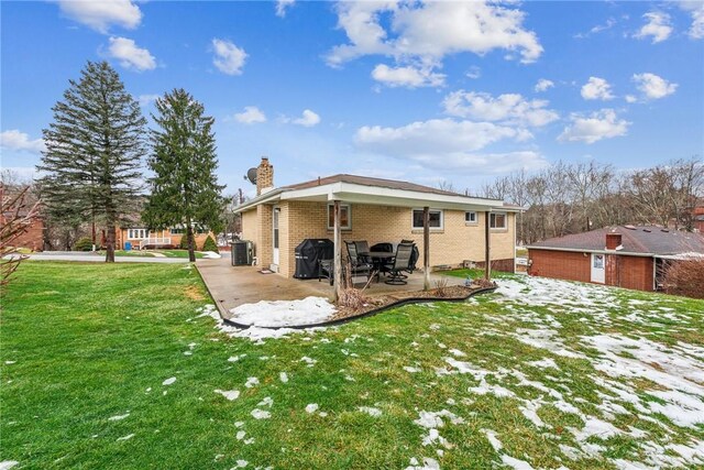 rear view of house featuring brick siding, a yard, a patio, a chimney, and central AC unit