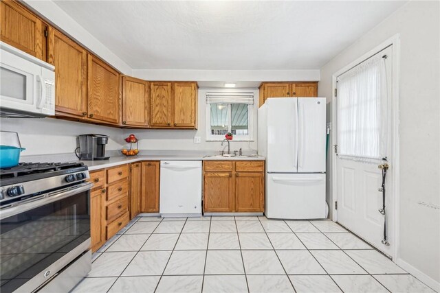 kitchen with brown cabinets, white appliances, light countertops, and a sink