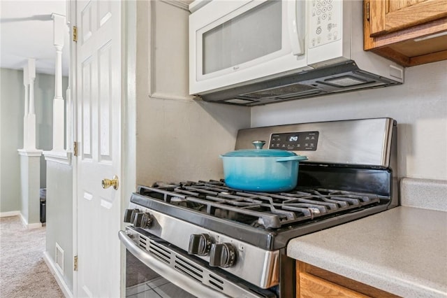 kitchen featuring light colored carpet, white microwave, brown cabinets, light countertops, and stainless steel range with gas stovetop