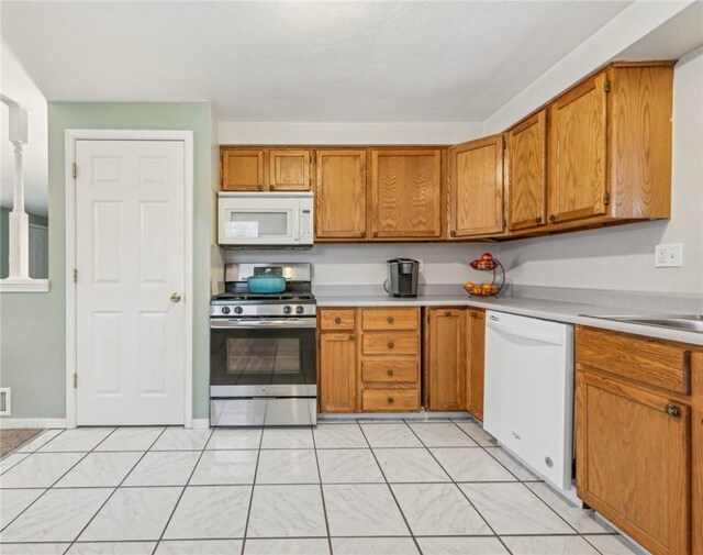 kitchen with brown cabinets, white appliances, light countertops, and a sink