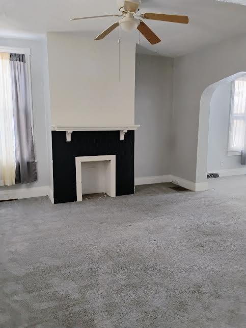 unfurnished living room with light colored carpet and ceiling fan