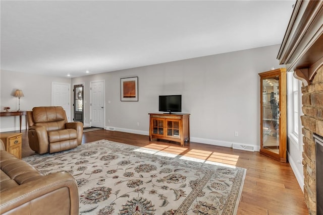 living room with a stone fireplace and light wood-type flooring