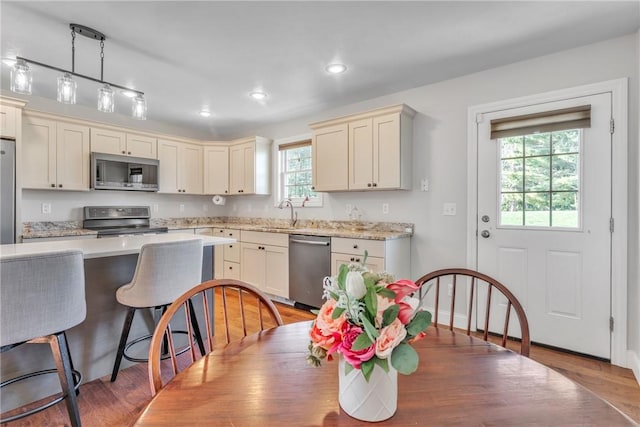 kitchen with stainless steel appliances, cream cabinets, light hardwood / wood-style floors, and decorative light fixtures