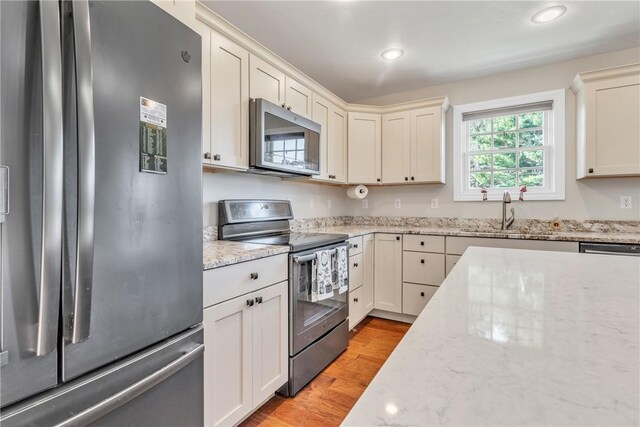 kitchen with light stone counters, appliances with stainless steel finishes, sink, and light hardwood / wood-style flooring