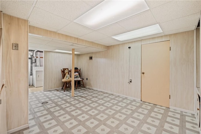 basement with washer / clothes dryer, a drop ceiling, and wooden walls