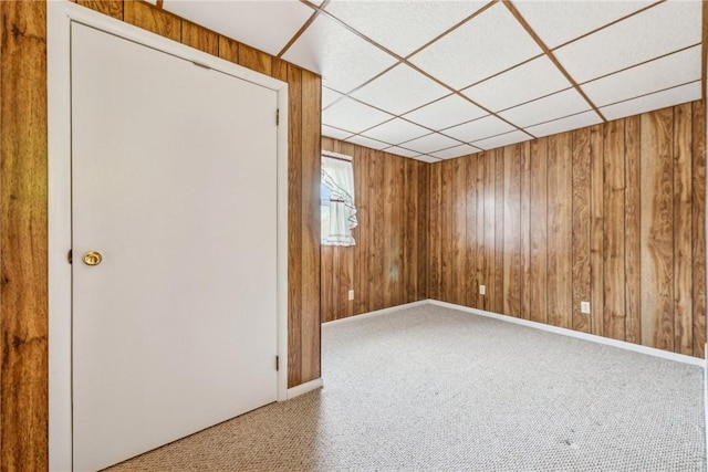 carpeted empty room featuring a drop ceiling and wooden walls