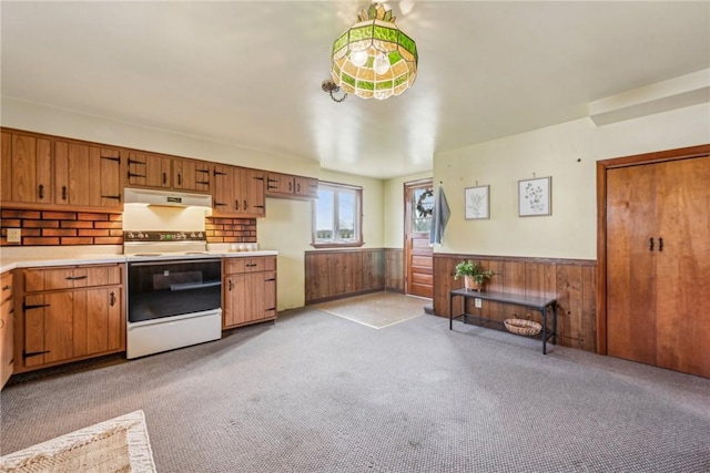 kitchen with light carpet, electric range, and wood walls