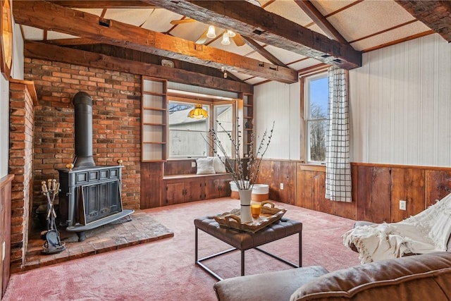 unfurnished living room with wooden walls, lofted ceiling with beams, carpet flooring, a wood stove, and ceiling fan