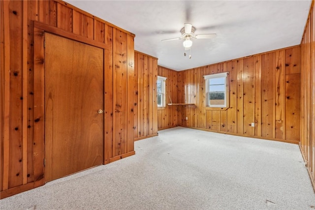 unfurnished room with light carpet, wooden walls, and ceiling fan