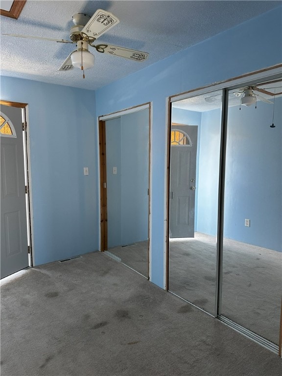 unfurnished bedroom with ceiling fan, two closets, a textured ceiling, and carpet flooring