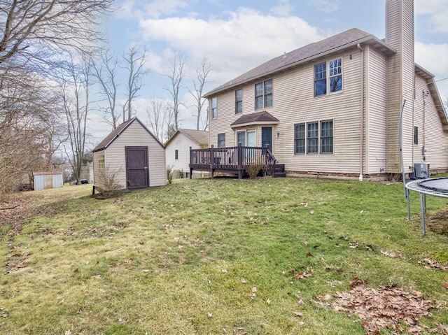 rear view of property with a shed, a wooden deck, a yard, and a trampoline