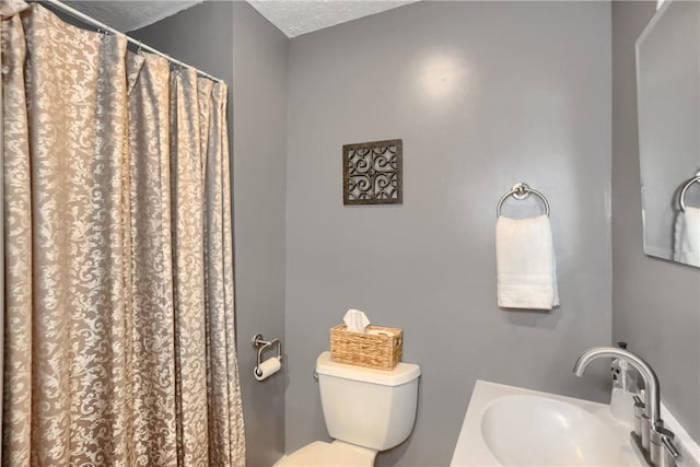 bathroom featuring walk in shower, toilet, sink, and a textured ceiling