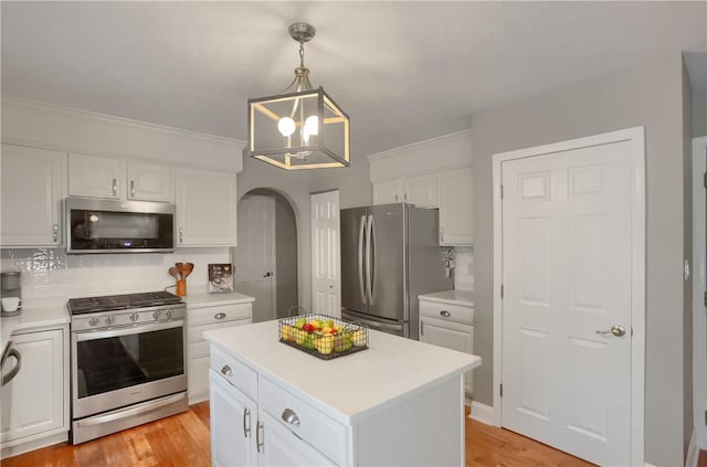 kitchen featuring appliances with stainless steel finishes, backsplash, a center island, white cabinets, and decorative light fixtures