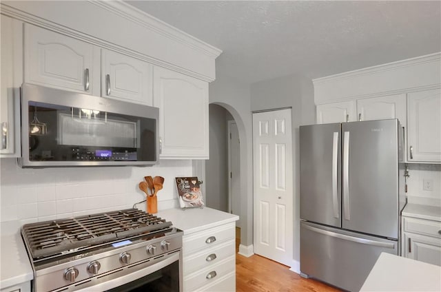 kitchen featuring appliances with stainless steel finishes, white cabinetry, ornamental molding, light hardwood / wood-style floors, and decorative backsplash