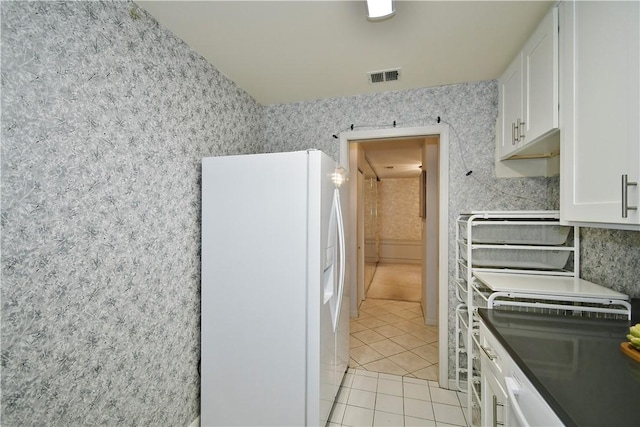 kitchen with white refrigerator with ice dispenser, light tile patterned floors, and white cabinets