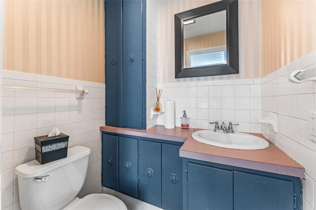 951 Buffalo St, City Of Franklin, PA 16323 - half bathroom with wallpapered walls, toilet, vanity, tile walls, and wainscoting