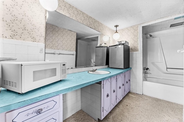 bathroom with vanity, tile walls, bathing tub / shower combination, and a textured ceiling