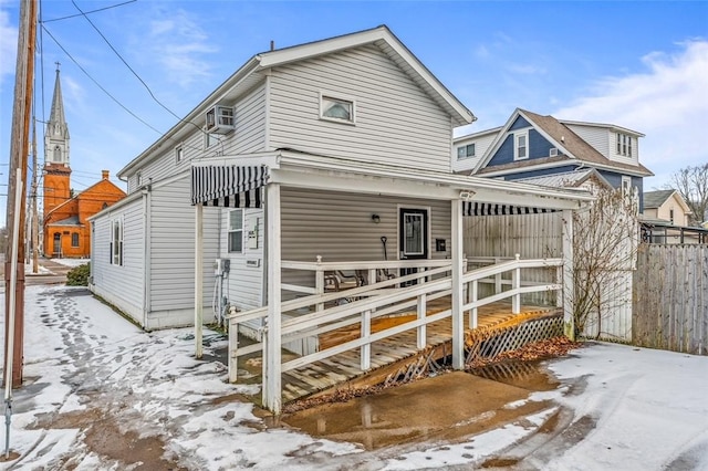 snow covered house with a wall mounted AC and covered porch