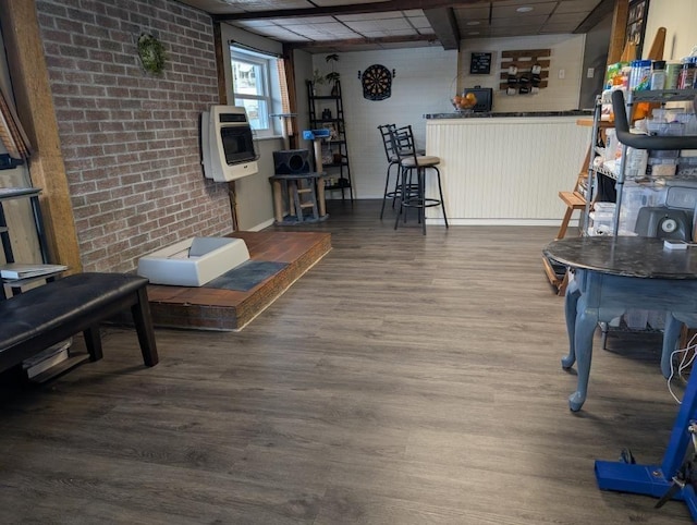 living room featuring brick wall, wood-type flooring, a paneled ceiling, and heating unit