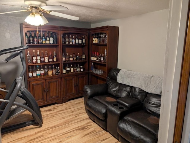 wine room featuring ceiling fan, a textured ceiling, bar area, and light wood-type flooring