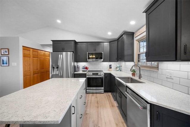 kitchen featuring light stone counters, vaulted ceiling, a center island, and appliances with stainless steel finishes