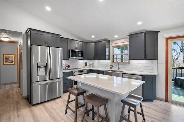 kitchen featuring a kitchen island, sink, a kitchen breakfast bar, stainless steel appliances, and light stone countertops