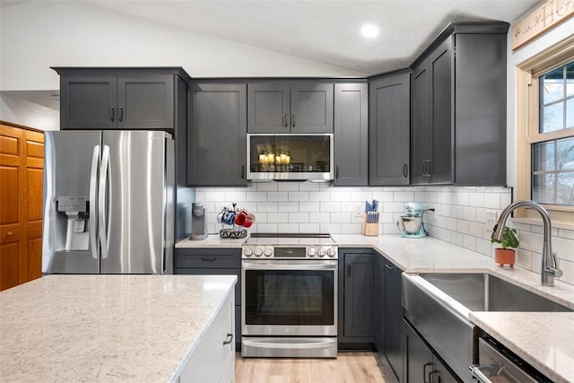 kitchen featuring lofted ceiling, sink, appliances with stainless steel finishes, light stone countertops, and light hardwood / wood-style floors