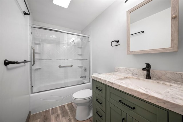 full bathroom featuring hardwood / wood-style flooring, vanity, toilet, and shower / bath combination with glass door