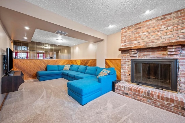 living room featuring a brick fireplace, wooden walls, a textured ceiling, and carpet flooring