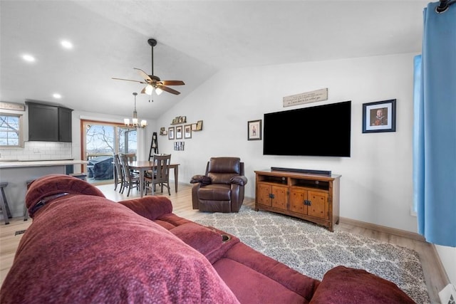 living room with lofted ceiling, ceiling fan with notable chandelier, and light hardwood / wood-style flooring