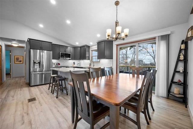 dining room with lofted ceiling, an inviting chandelier, and light wood-type flooring