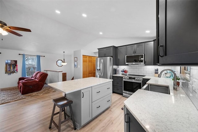 kitchen with sink, stainless steel appliances, light stone counters, a kitchen bar, and decorative light fixtures