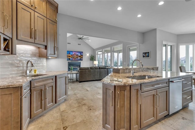 kitchen with sink, vaulted ceiling, light stone countertops, and a center island with sink