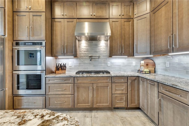 kitchen with light stone counters, appliances with stainless steel finishes, range hood, and backsplash