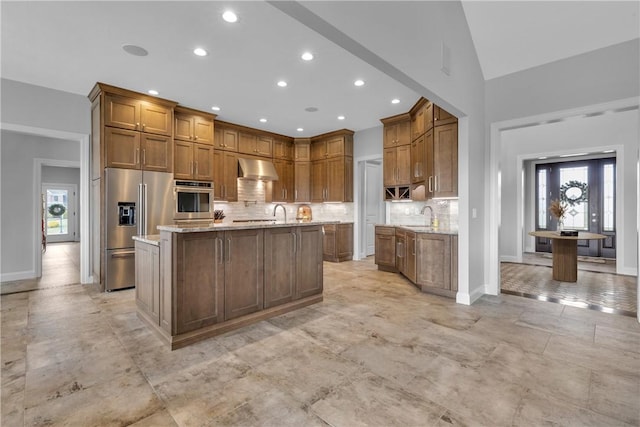 kitchen featuring light stone counters, appliances with stainless steel finishes, an island with sink, and backsplash