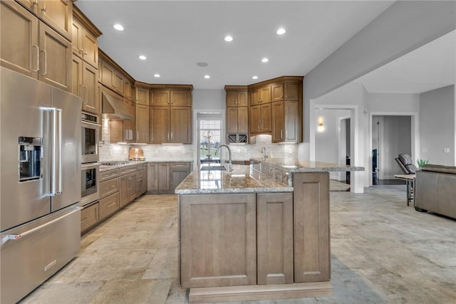 kitchen with extractor fan, appliances with stainless steel finishes, sink, backsplash, and light stone counters