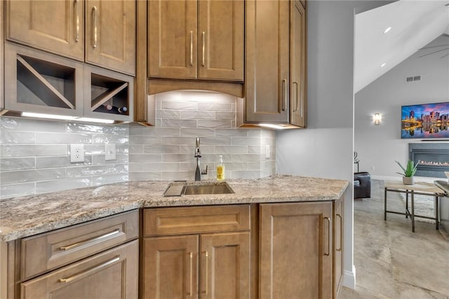 kitchen featuring light stone countertops, sink, lofted ceiling, and decorative backsplash