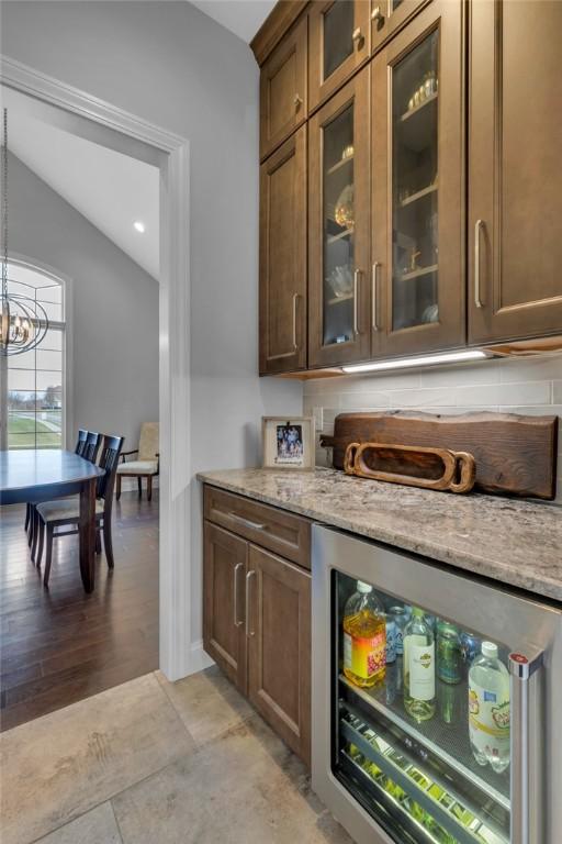 bar featuring pendant lighting, wine cooler, a notable chandelier, light stone countertops, and vaulted ceiling