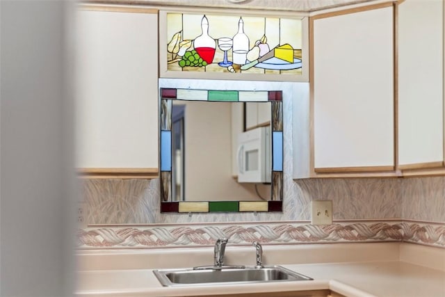 interior space featuring white microwave, a sink, light countertops, white cabinetry, and backsplash