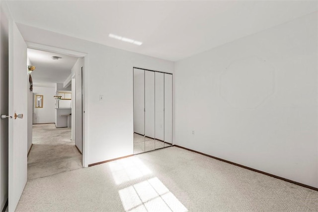 unfurnished bedroom with baseboards, a closet, and light colored carpet