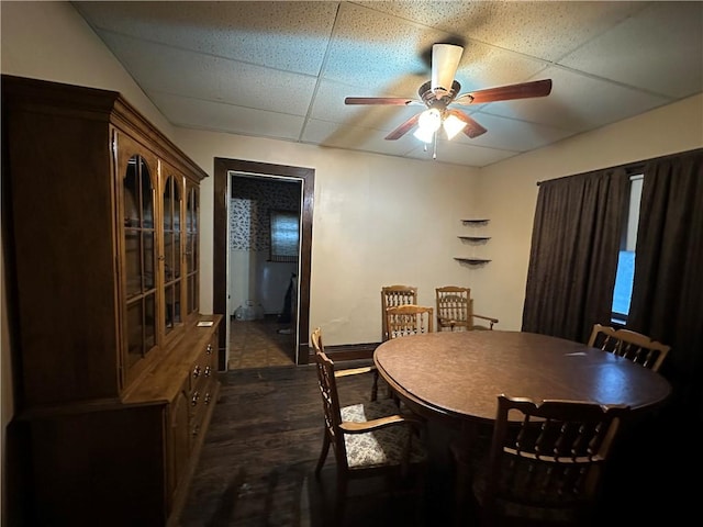 dining space featuring a drop ceiling, dark wood-type flooring, and ceiling fan