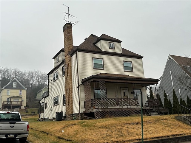 front facade with cooling unit, covered porch, and a front yard