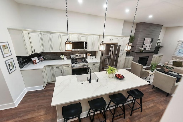 kitchen featuring a breakfast bar area, hanging light fixtures, a kitchen island with sink, light stone counters, and stainless steel appliances