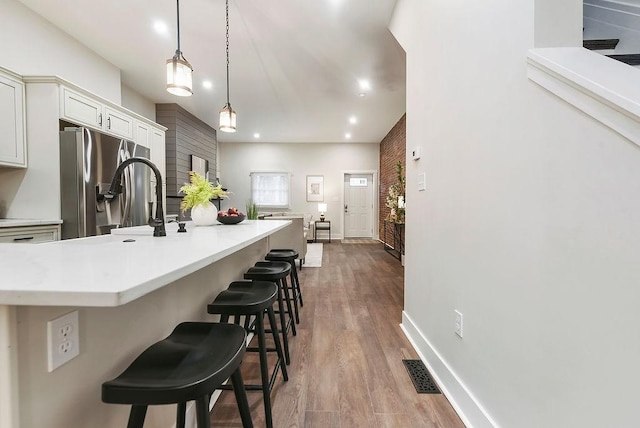 kitchen with pendant lighting, a breakfast bar area, white cabinets, stainless steel refrigerator with ice dispenser, and light hardwood / wood-style flooring